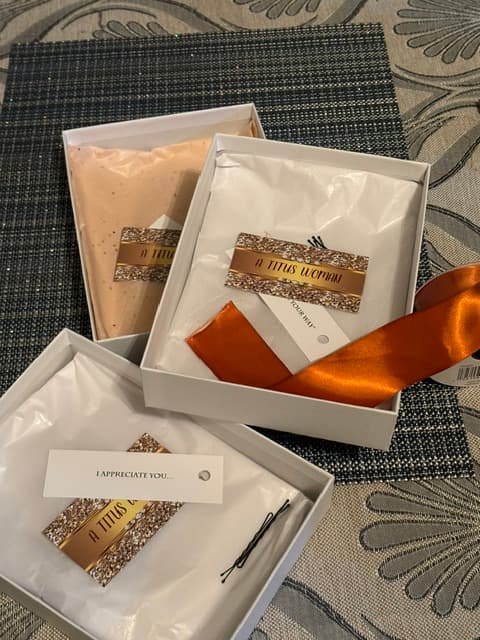 Three white gift boxes with tissue wrapped items, gold branded cards, and an orange ribbon.