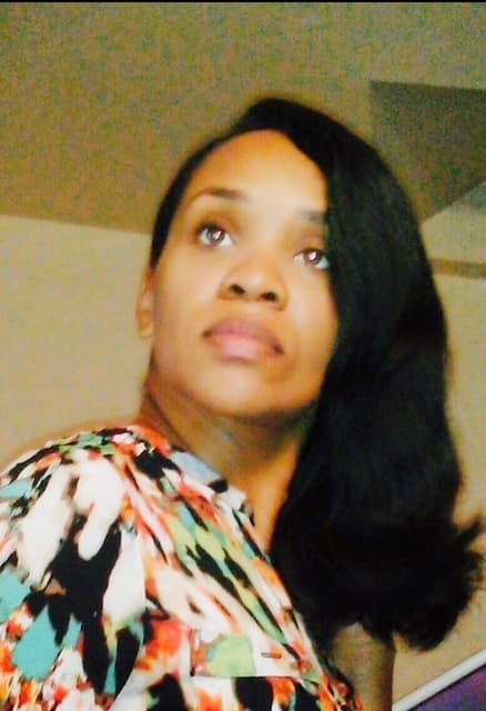 Woman with long dark wavy hair looking upwards wearing a colorful abstract patterned blouse.