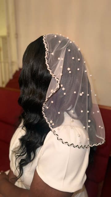 Short white sheer veil with pearls and braided trim over long wavy dark hair.