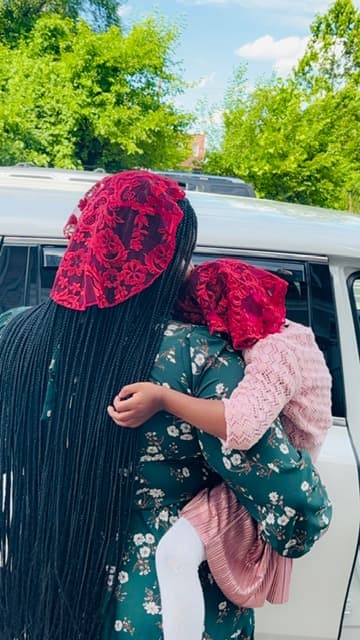 Woman with long braids holding a child, both wearing matching red lace head coverings.